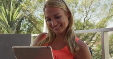 Genç, beyaz bir kadının yaz tatilinde balkondaki bir masada oturup, ağır çekimde tablet kullanmasının ön görüntüsü..