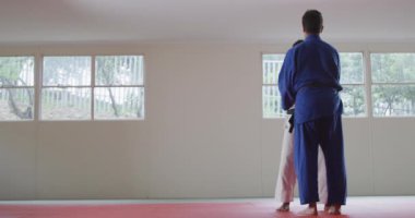 Karışık ırk erkek judo koçu ve genç karışık ırk judokası, mavi-beyaz judogi giyen, spor salonunda judo antrenmanı yapan genç, koçu ağır çekimde mindere fırlatıyor..
