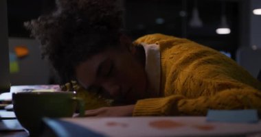 Modern bir ofiste geç saatlere kadar çalışan, kahve fincanının başında uyuyan, uyanıp bilgisayar ekranına bakan yorgun bir iş kadınının yan görüntüsü.