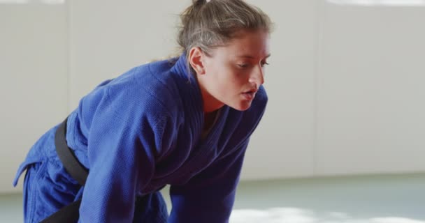 青い柔道衣を着た10代の白人女性柔道選手の側面図 スローモーションで柔道の訓練の前にジムのマットに立って — ストック動画