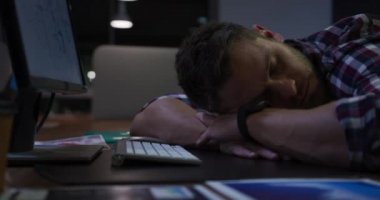 Modern bir ofiste geç saatlere kadar çalışan, bilgisayar klavyesinin yanında uyuyan yorgun, beyaz bir işadamının yan görüntüsü.