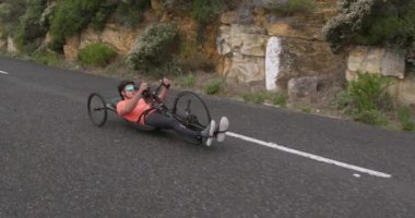 Spor kıyafetleri içinde beyaz bir adamın yan görüntüsü. Açık havada antrenman yapıyor, bisiklete biniyor, yavaş çekimde sakin bir kır yolunda bisiklet sürüyor.