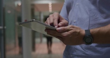 Modern bir ofiste geç saatlere kadar çalışan beyaz bir işadamının ön tarafı. Bir tablet bilgisayar kullanarak koridorda duruyor. Kadın meslektaşı arka planda yürüyor.