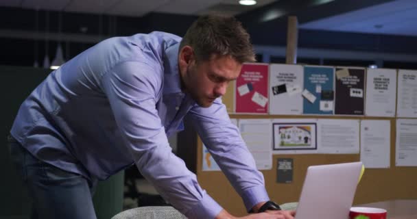 一个全神贯注的白人商人在一间现代化的办公室工作到很晚 用笔记本电脑站在办公桌旁 看着电脑屏幕的侧视图 — 图库视频影像