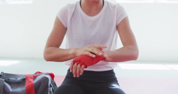 一个年轻的白种人女子柔道运动员坐在体育馆的垫子上 慢吞吞地在手腕上缠着红色的带子 — 图库视频影像