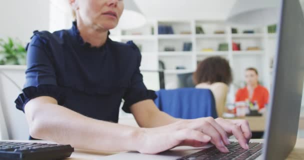 一个在现代办公室工作的白人女商人坐在她的办公桌前 用笔记本电脑和她的同事们一起慢动作地在后台工作 — 图库视频影像