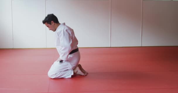 一名身穿白色柔道的混合型男子柔道教练跪在体育馆的垫子上 然后慢动作地进行柔道训练 — 图库视频影像