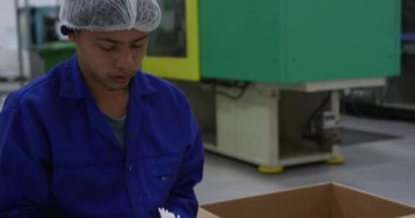 Yoğun bir fabrika deposunda çalışan, saç filesi ve tulum giyen, plastik parçaları hazırlayan ve paketleyen karışık ırk erkek işçilerinin ön görüntüsü.