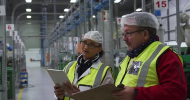 Kafkas erkek ve kadın işçilerin yoğun bir fabrika deposunda çalışırken, saç filesi ve yüksek görünürlüklü yelekler giyerken, tablet bilgisayar kullanırken ve birlikte tartışırken yan görüntüler.