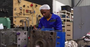 Bir fabrika atölyesinde oturan, saç filesi takan ve metal parçaları hazırlayan ve kontrol eden Afrikalı Amerikalı erkek işçilere yan bakış.