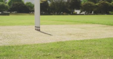 Beyaz giyimli, beyaz tenli, beyaz tenli, beyaz tenli, kriket maçında sahada topu atmak için koşan, arka planda koşmaya hazırlanan bir vurucunun yan görüntüsü.