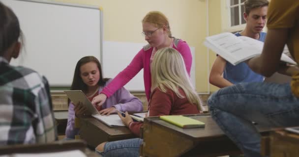 教室で本やタブレットコンピュータを使って学び 交流し 協力し ゆっくりと動き回る10代の男女の高校生の多民族グループのフロントビュー — ストック動画