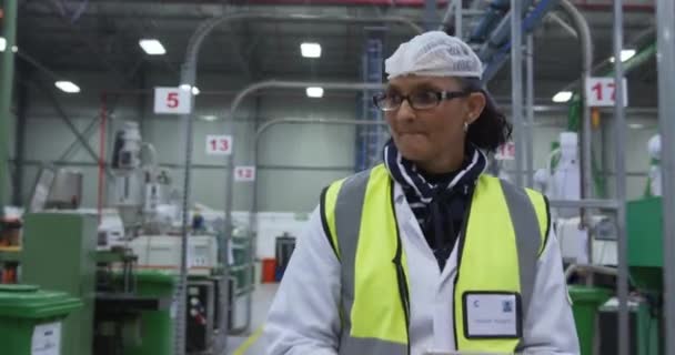 在繁忙的工厂仓库工作 戴着眼镜 戴着发网 身穿高光背心 使用平板电脑 穿过工厂仓库进行检查的专注的白人女工的前景 — 图库视频影像