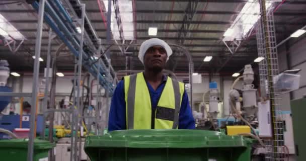 忙しい工場倉庫で働くアフリカ系アメリカ人男性労働者の正面図 ヘアネットを身に着けています 全体と視認性の高いベスト 緑のビンをプッシュ工場で歩いて — ストック動画