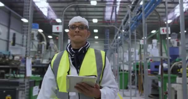 在一家繁忙的工厂仓库里工作 戴着眼镜 戴着发网 身穿高光背心 使用平板电脑 穿过工厂仓库进行检查的专注的白人女工的近视 — 图库视频影像