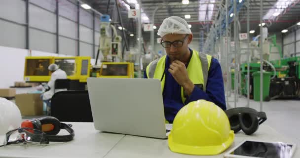 在繁忙的工厂仓库工作 身穿发网和高能见度背心 坐着和使用手提电脑的专注的混血男工的前景 — 图库视频影像