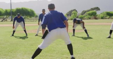 Kafkasyalı bir erkek beyzbol koçunun antrenman sırasında çok ırklı bir erkek beyzbol takımına antrenman yapmasını, maçtan önce hazırlanmasını, güneşli bir günde beyzbol sahasında yavaş çekimde antrenman yapmasını,