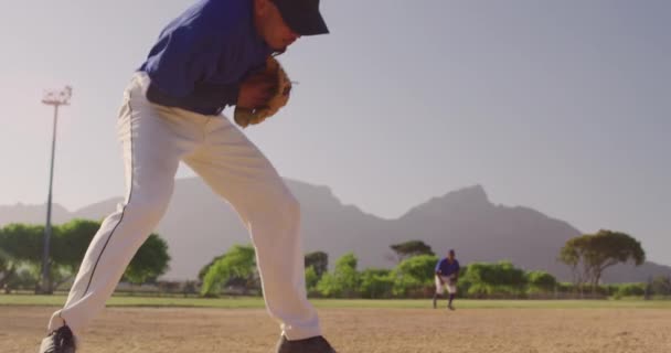 在阳光灿烂的日子里 在一场棒球比赛中 一个混合种族的男性棒球手的侧视图 他带着手套接住一个球 并以慢动作将球抛出 而他的队友则在后面 — 图库视频影像