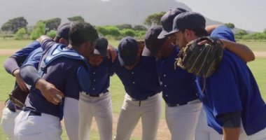 Erkek beyzbol oyuncularından oluşan çok ırklı bir takımın yan görüntüsü, maçtan önce, bir beyzbol sahasında toplanmış, güneşli bir güne, ağır çekimde odaklanıyorlar.