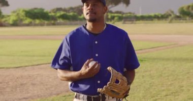 Güneşli bir günde beyzbol sahasında duran, eldiven takan, topla oynayan ve ağır çekimde gülümseyen melez bir erkek beyzbol oyuncusunun portresi.