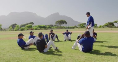 Kafkasyalı bir erkek beyzbol koçunun oyun sahasında durup çok ırklı beysbol oyuncularına antrenman yaptırması, maçtan önce antrenman yapması güneşli bir günde ağır çekimde mekik çekmesi.