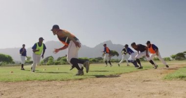 Çok ırklı beysbol oyuncularından oluşan bir grubun düşük açılı görüntüsü, antrenmanlarını sahada yapıyorlar, kısa mesafe koşuları yapıyorlar, güneşli bir günde yavaş çekimde dönüyorlar.