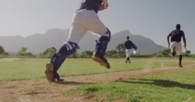 Çok ırklı erkek beyzbol oyuncularından oluşan bir grubun arka planda, maçtan önce hazırlanmaları, antrenman yapmaları, antrenman yapmaları, güneşli bir günde arka planda koçlarıyla ağır çekimde koşmaları.