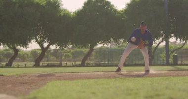 Güneşli bir günde beyzbol maçı sırasında, karışık ırktan bir erkek beyzbol oyuncusunun, eldiveniyle düşük bir topu yakalayıp, yavaş çekimde attığını görmek.