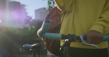 Güneşli bir günde akıllı telefonunu kullanarak şehirde takılan ve bisikletini yavaş çekimde kullanan modaya uygun bir transseksüel yetişkinin ön görüntüsü..