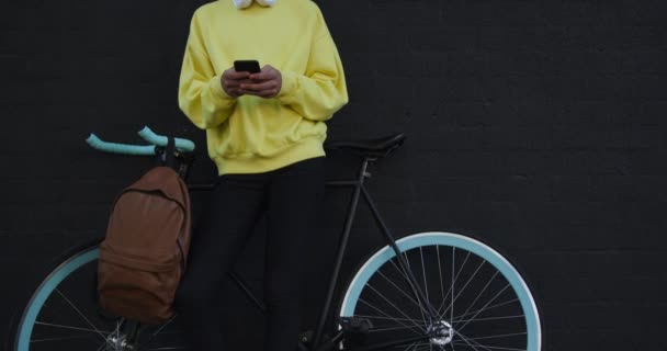 都会の夏の日に自転車で通りに立ちスローモーションでスマートフォンを使っているトランスジェンダーの大人のファッショナブルな混合レースのフロントビュー — ストック動画