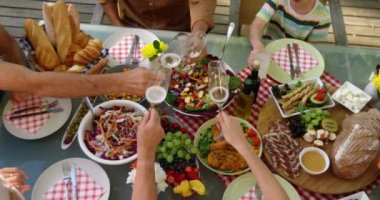 Kutlama yemeği için yemek masasının önünde oturan, kadehleri kaldıran ve kadeh kaldırmak için masaya uzanan çok nesilli beyaz bir ailenin yüksek açılı görüntüsü.