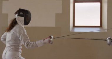 Beyaz ırktan beyaz bir bayan eskrim sporcusu spor salonunda eskrim eğitimi alırken, eskrim müsabakalarında maske takarak antrenman yaparken, çengelleriyle birbirlerine nişan alırken, bir kadın yavaş çekimde rakibi tarafından pipisinin yere fırlatılması...