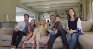 Oturma odasındaki kanepede oturup televizyon izleyen, zafer için tezahürat yapan ve yumruklarını şaklatan çok nesilli beyaz bir ailenin altı üyesinin alçak açılı ön görüntüsü.