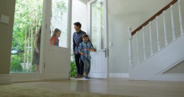 Kafkasyalı bir çiftin ve genç oğullarının yeni evlerinin ön kapısından girerken düşük açılı görüntüsü var. Çocuklar ağır çekimde önde koşuyor.