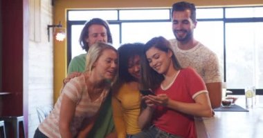 Gün boyunca bardaki çok ırklı erkek ve kadın arkadaşlardan oluşan bir grubun önünde elinde akıllı bir telefon olan bir kadın, birlikte gülümseyip gülerken çekilmiş bir selfie çekiyor.