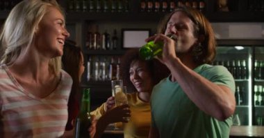 Barda içki içen, eğlenen, kutlayan, gülümseyen ve birlikte ağır çekimde gülen beş farklı etnik gruptan oluşan bir grubun önünde.