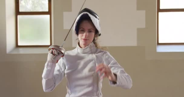 一名专注的白人女子击剑运动员穿着手套 斑纹和面罩站在体育馆接受击剑训练 慢吞吞地在肩上撒尿的形象 — 图库视频影像