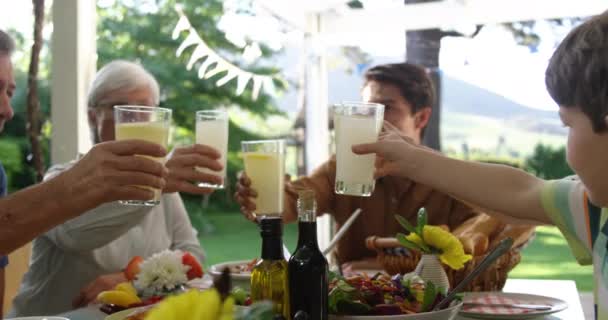 複数世代の白人の家族の近くのサイドビューは 食事のためのディナーテーブルセットの外に座って グラスを上げ テーブルを横切って到達し トーストを作り スローモーション — ストック動画