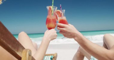 Sahilde yan yana oturup mavi gökyüzü ve denizin olduğu kokteylleri yudumlayan, kumsalda birlikte vakit geçirmeyi seven mutlu, beyaz bir çiftin arka plan görüntüsü.