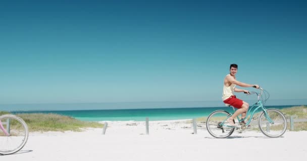 一緒にビーチで自由な時間を楽しんで幸せな白人のカップルのサイドビュー 彼らのバイクの話に乗って 遅い動きで背景に青い空と海を持つ男に続く女性 — ストック動画