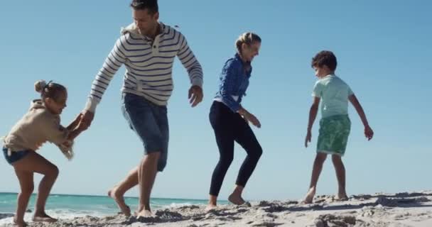 一緒にビーチで自由な時間を楽しんでいる彼らの息子と娘と一緒に白人のカップルの低角度側のビュー ランニング 手を握って スローモーションで背景に海と青い空と遊ぶ — ストック動画
