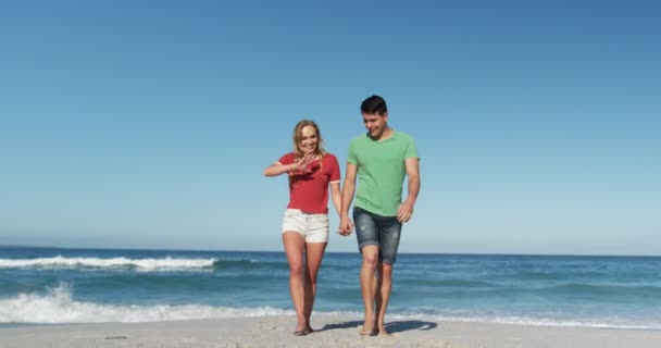 一对快乐的白种人情侣在沙滩上共度时光 手牵着手在蓝天和大海中慢悠悠地走着 眼前的景象是这对恋爱中快乐的白种人夫妇 — 图库视频影像