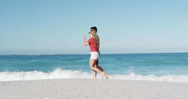 一对恋爱中的快乐的高加索夫妇在沙滩上享受着闲暇时光 在慢镜头的背景下与蓝天和大海手牵手散步 — 图库视频影像