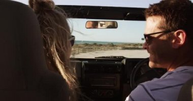 Kafkasyalı bir çiftin yol gezisi sırasında boş zaman geçirmesini arka planda mavi gökyüzü ve denizle birlikte yavaş çekimde, açık bir arabanın içinde oturup gülümsemelerini.