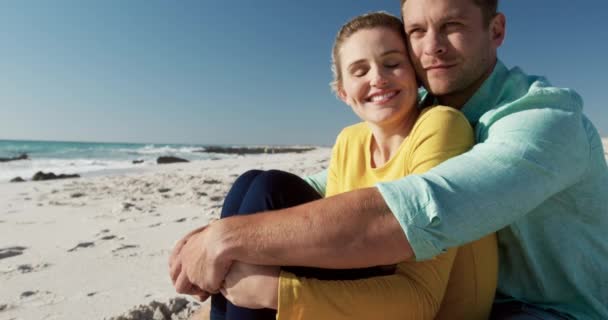 ビーチで一緒に自由な時間を楽しむことを愛する白人のカップルのフロントビューの近くに 砂の上に座って スローモーションの背景にある海と青い空を受け入れる — ストック動画