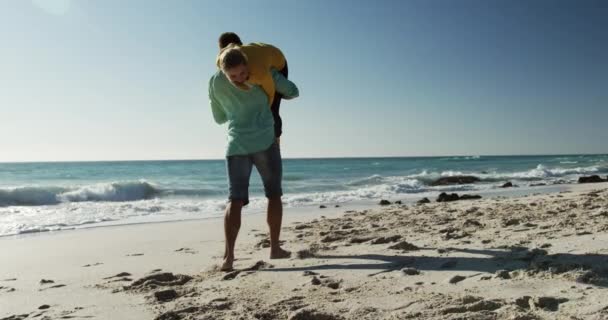 一对相恋的白种人在沙滩上享受着悠闲的时光 男人慢吞吞地把女人抱在肩上 身后是大海和蓝天 — 图库视频影像