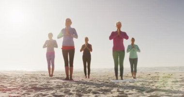 Güneşli bir günde kumsalda boş vakit geçiren bir grup beyaz kadın arkadaşın ön görüntüsü. Ağır çekimde yoga yapıyorlar.