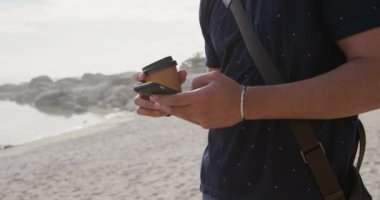 Güneşli bir günde doğada boş zamanların tadını çıkaran melez bir ırkın orta kesiminde akıllı telefon kullanarak kahveyi yavaş çekimde tutuyor.