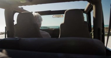 Son sınıf beyaz bir çiftin araba yolculukları sırasında arabalarında oturup, güneşin altında sahile giderken, direksiyondaki adamın arka görüntüsü.