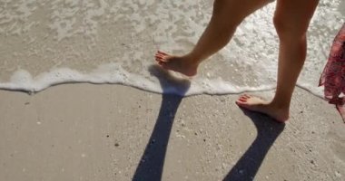 Deniz kenarında güneşli bir sahilde yürüyen genç bir melez kadının yan görüntüsü.